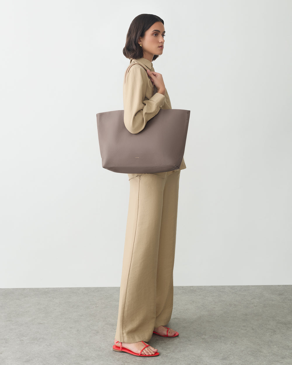 Person in outfit holding large tote bag, standing on a gray surface.