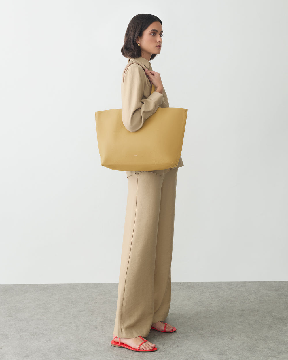 Person in outfit holding large tote bag, standing sideways.