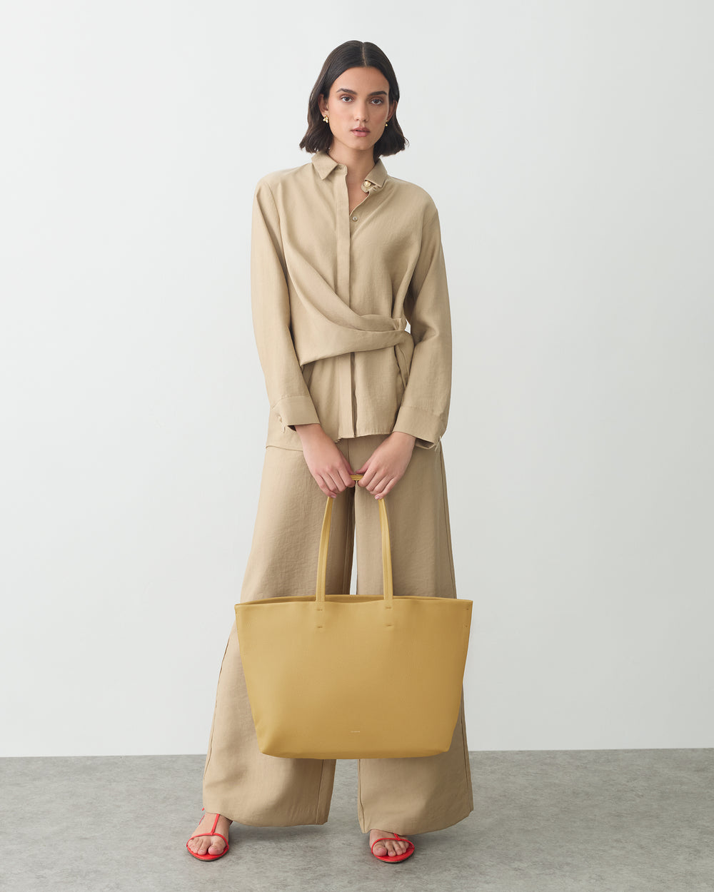 Person in long-sleeve outfit holding a large tote bag in front of a plain background.