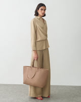 Person in an outfit holding a large handbag standing on a plain background.
