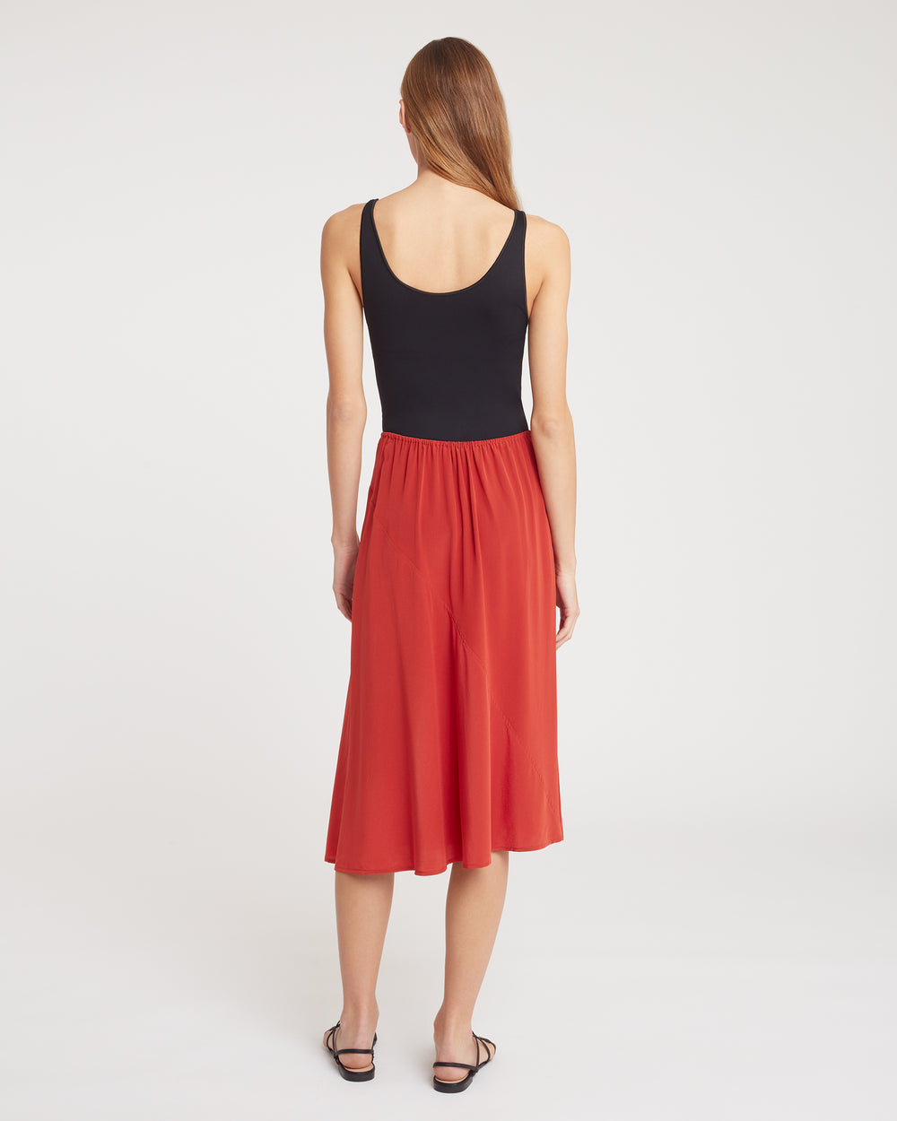 Person wearing a sleeveless top and midi skirt, standing with back turned.