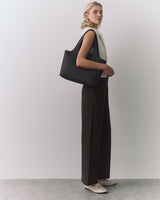 Person standing with large handbag over shoulder, wearing sleeveless top and wide-leg pants.