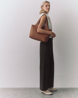 Person standing with a shoulder bag, wearing a sleeveless top and wide-leg pants.