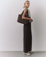 Person standing with a large handbag, wearing a sleeveless top and wide-leg pants.