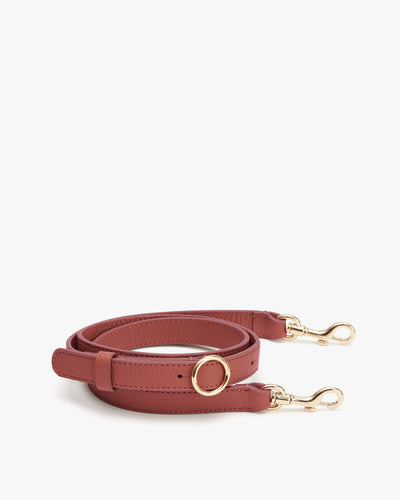 Leather strap with gold clips and adjustable buckle displayed on flat surface.