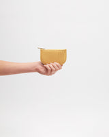 Hand holding small zippered pouch against plain background.