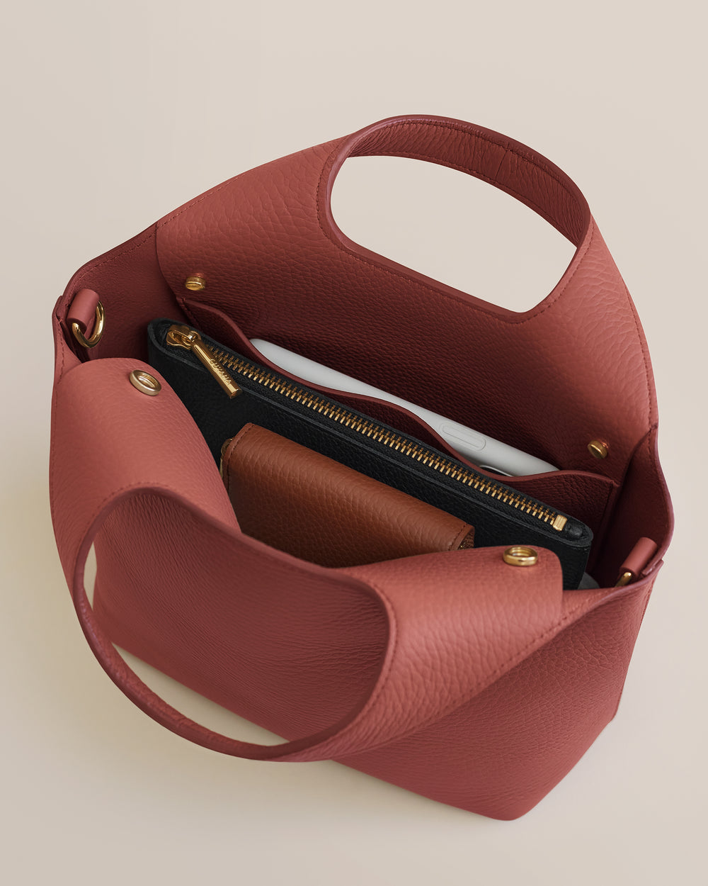 Top view of an open handbag showing contents like a clutch and notebook inside.