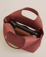 Top view of an open handbag showing contents like a clutch and notebook inside.