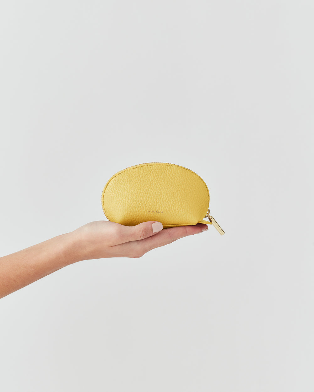 Hand holds a small half-moon pouch against a plain background.