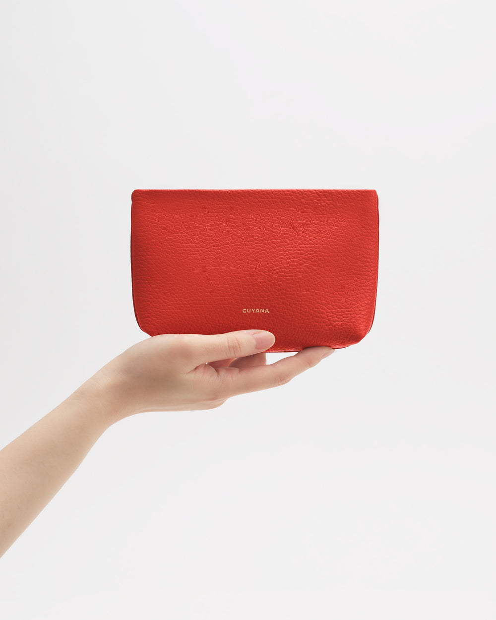 Hand holding a rectangular pouch against plain background.