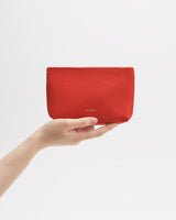 Hand holding a rectangular pouch against plain background.