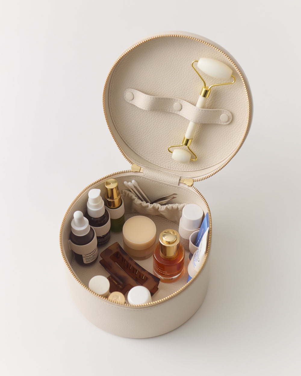 Round open case with skincare bottles and a facial roller inside.