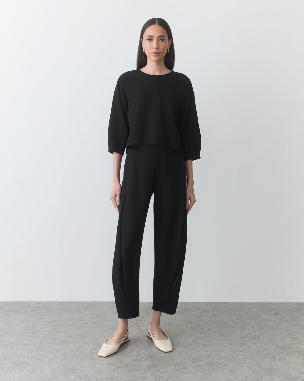 Person wearing a long-sleeve top and pants standing on a plain background.