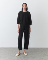 Person wearing a long-sleeve top and pants standing on a plain background.