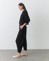 Person wearing a two-piece outfit and flat shoes, standing side profile in a plain room.