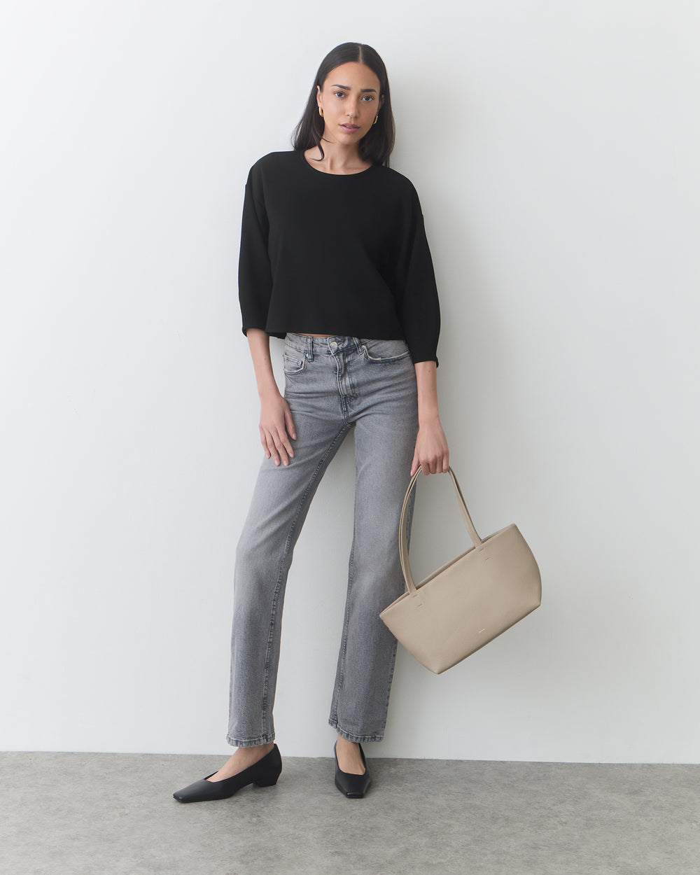 Person standing with a handbag, wearing a sweater, jeans, and shoes.