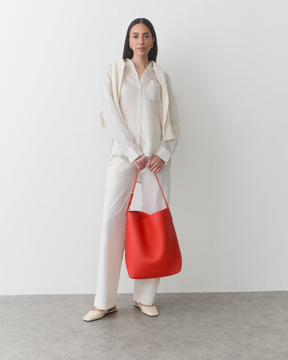 Woman standing in a neutral outfit carrying a brightly colored shoulder bag by its strap.