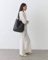 Woman carrying a shoulder bag on her shoulder against a plain background.