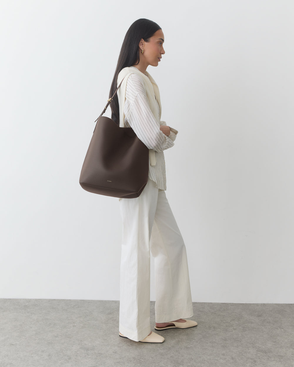Woman holding a shoulder bag on her shoulder while wearing a neutral outfit.