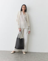 Woman wearing a neutral outfit carrying a statement shoulder bag against a plain background.