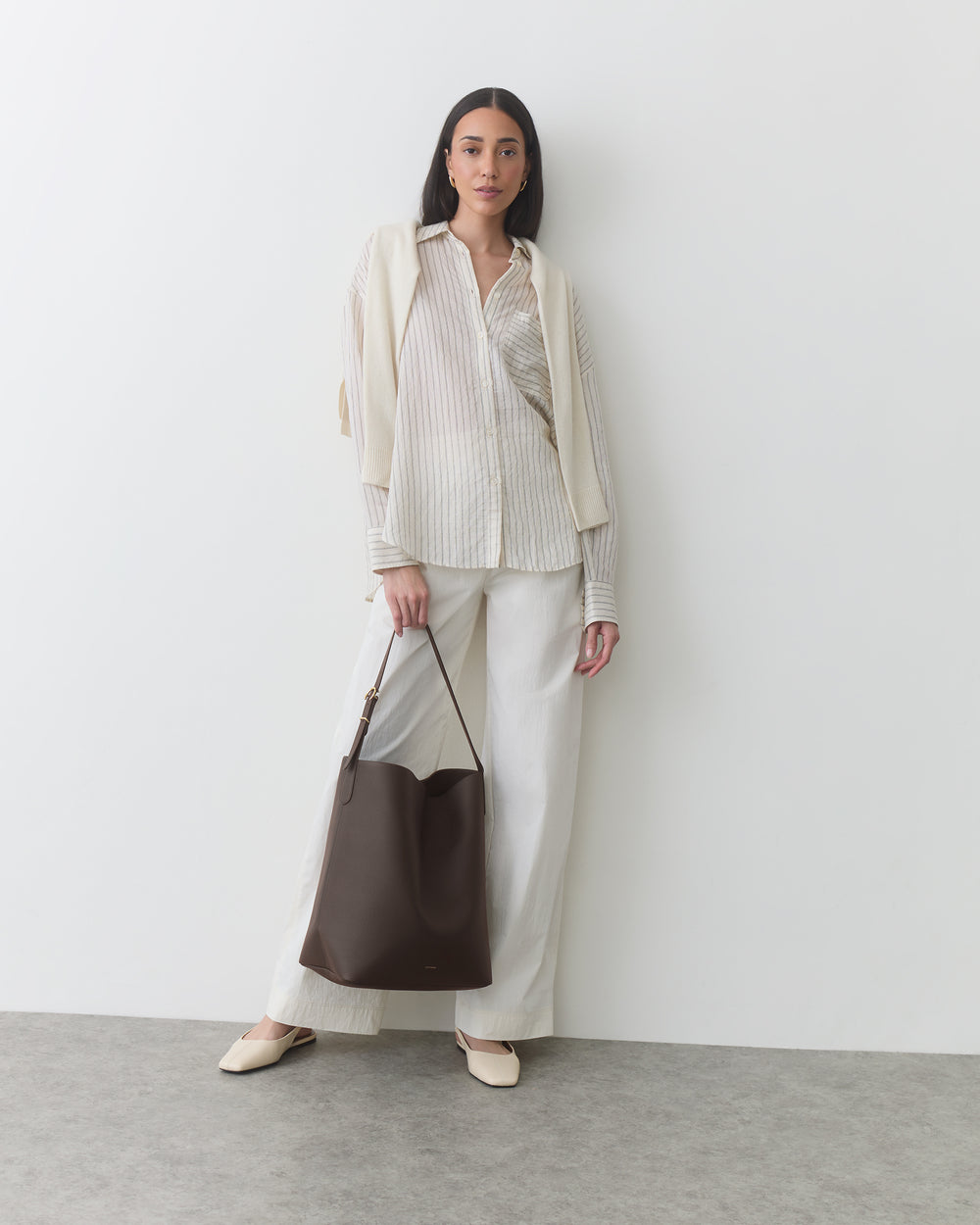 Woman wearing a neutral outfit carrying a shoulder bag in front of her body.