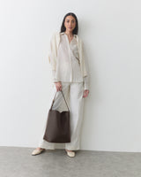 Woman wearing a neutral outfit carrying a shoulder bag in front of her body.