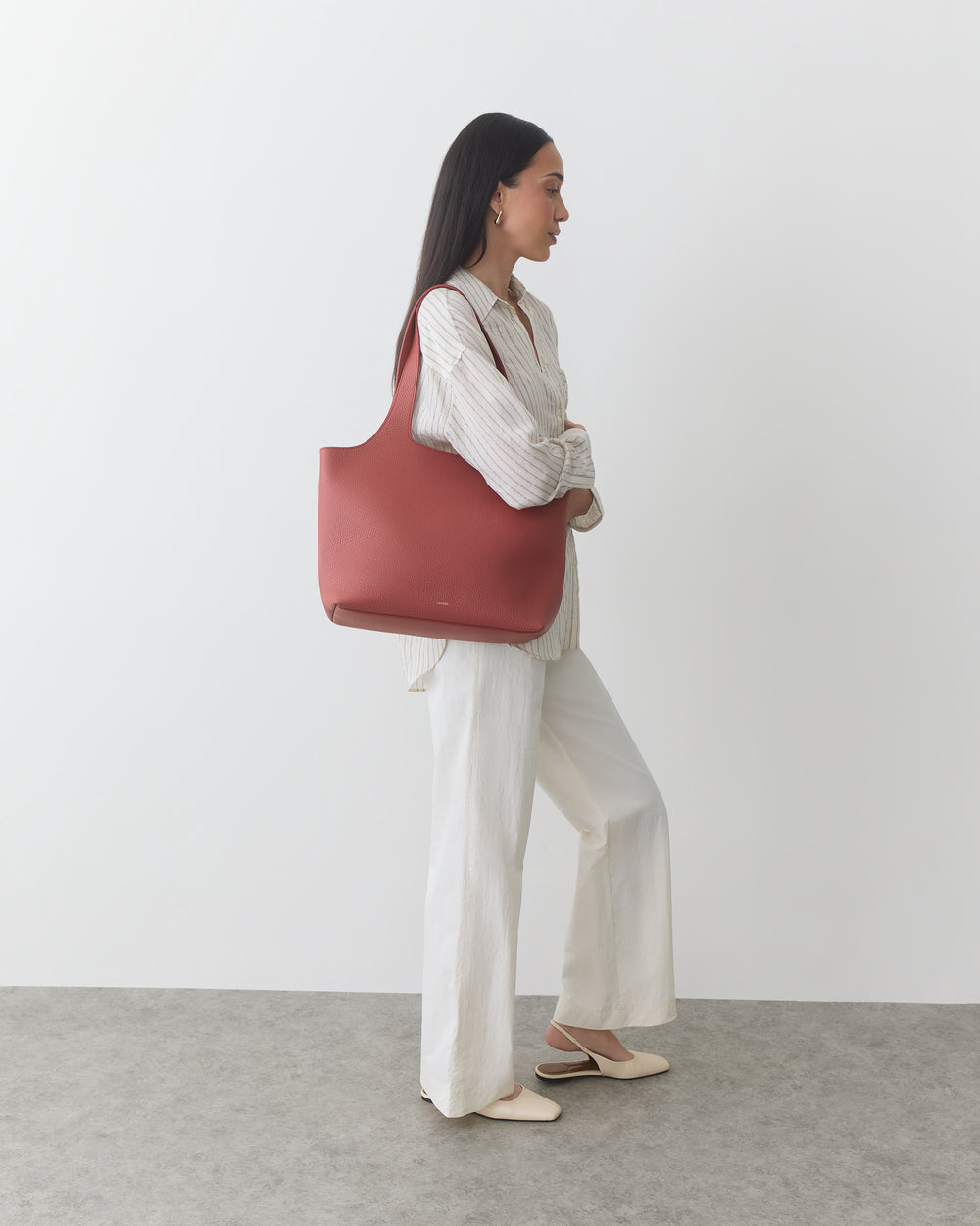Person standing with a shoulder bag, wearing a shirt and pants.