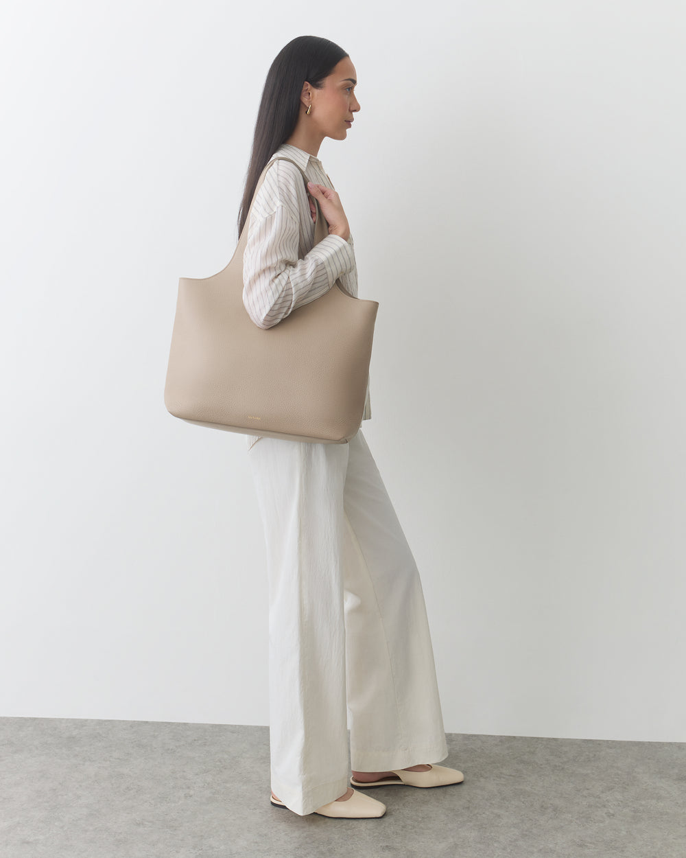 Person standing with large shoulder bag, wearing a long-sleeve shirt and wide-leg pants.