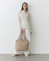 Person standing with a tote bag wearing a button-up shirt and pants.