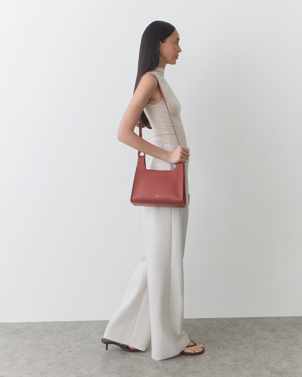 Person in sleeveless outfit carries shoulder bag and wears sandals.