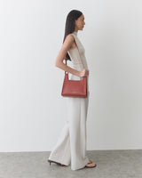 Person in sleeveless outfit carries shoulder bag and wears sandals.