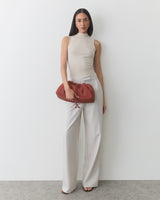 Person in sleeveless top and pants holding a gathered clutch bag.