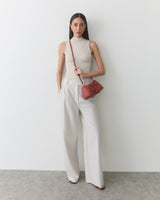 Person in sleeveless top and wide-leg pants holding a shoulder bag.