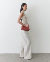Woman in sleeveless top and wide-leg pants holding a shoulder bag.