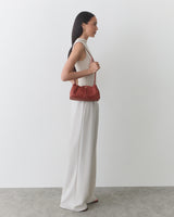 Person holding a handbag wearing sleeveless top and wide pants standing sideways