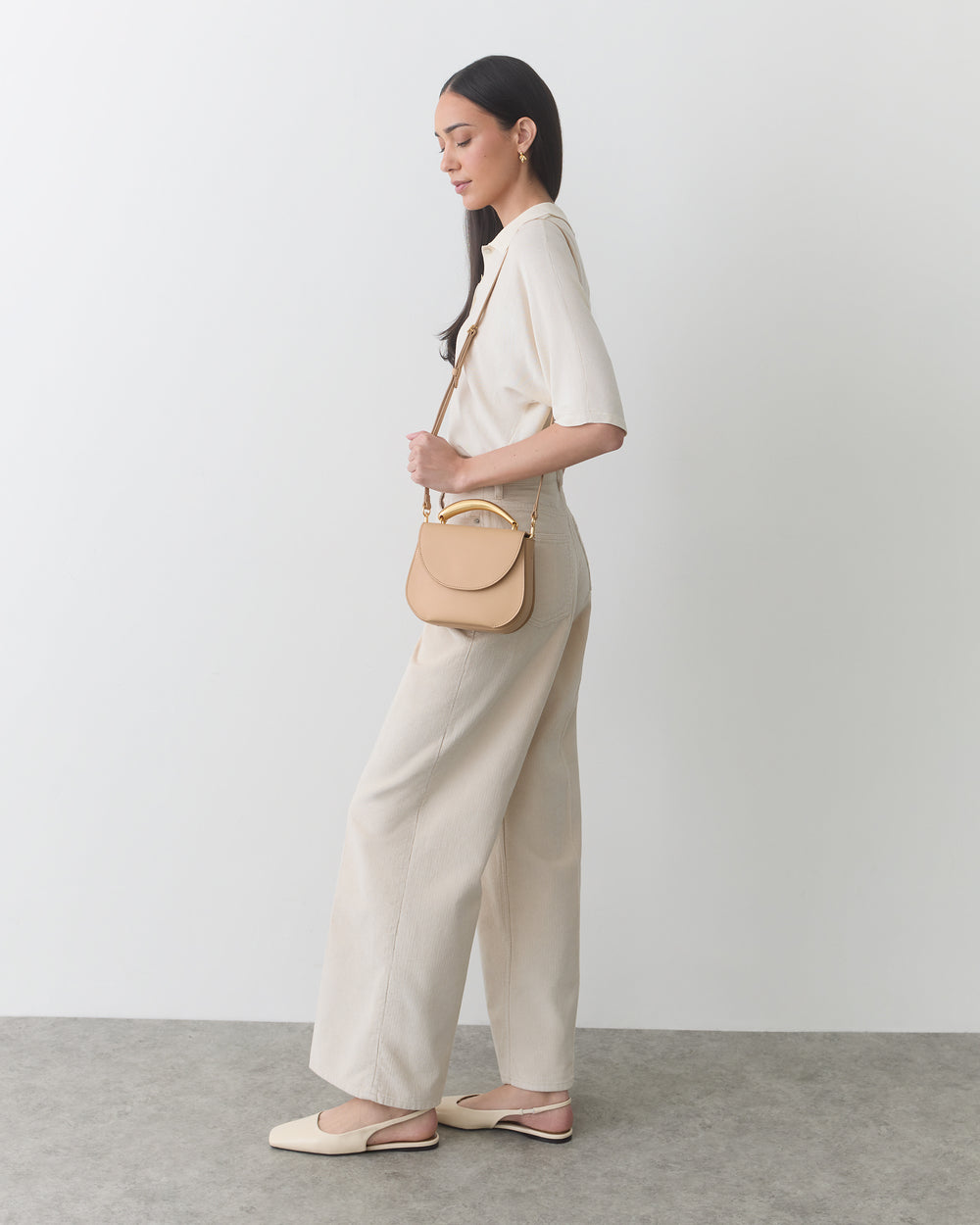 Person in a top and pants holds a handbag, standing against a plain background.