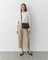 Person in sweater and pants with a crossbody bag, standing against a plain background.