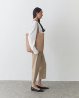 Person standing with tote bag wearing long-sleeve top, pants, and flat shoes.