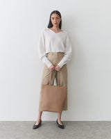 Woman standing with large tote bag, wearing sweater and wide-leg pants.