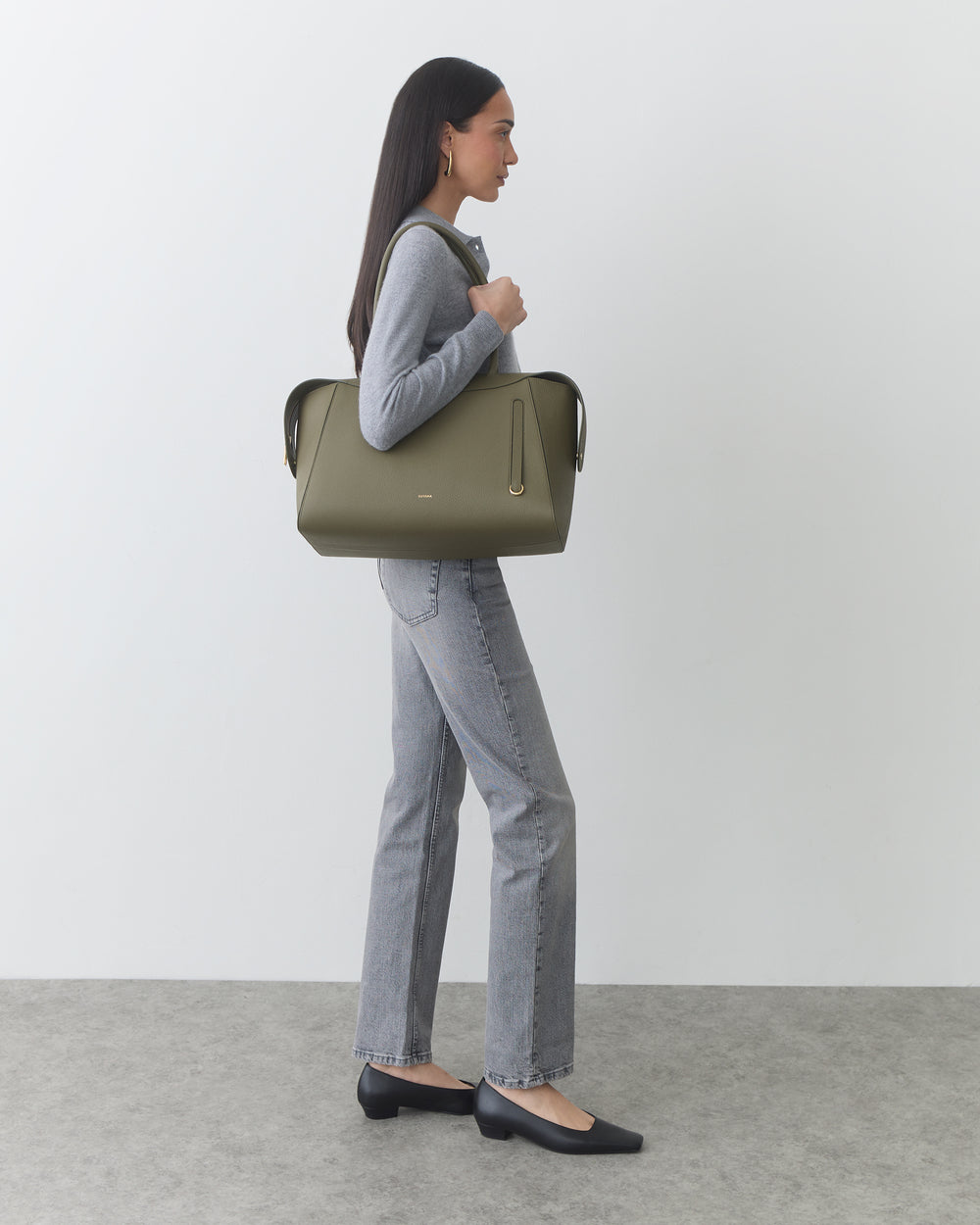 Person standing with large handbag wearing jeans and flats.