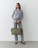 Person with travel bag wearing button-up shirt and jeans.