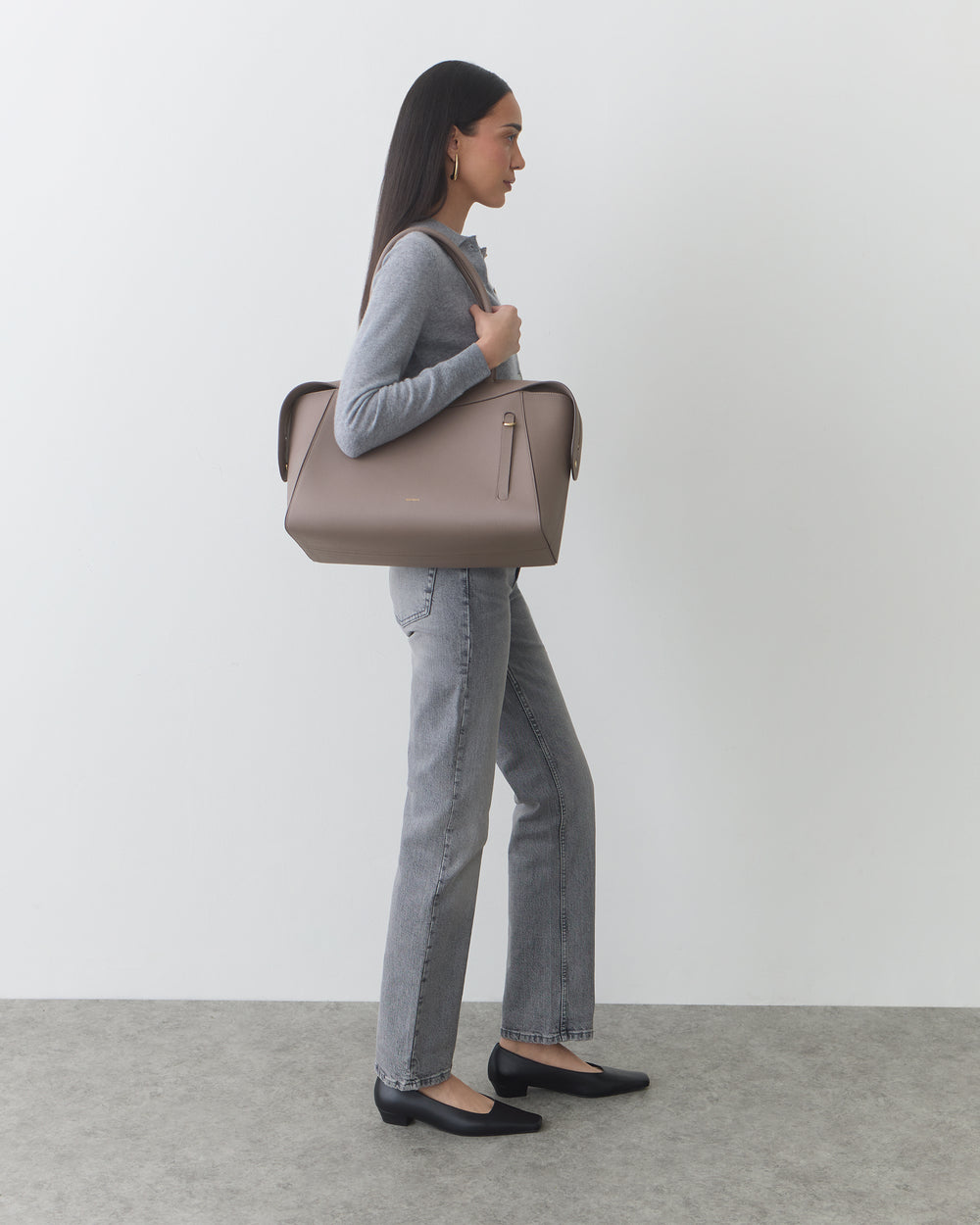 Person standing with a large travel bag, wearing a long sleeve top and jeans.