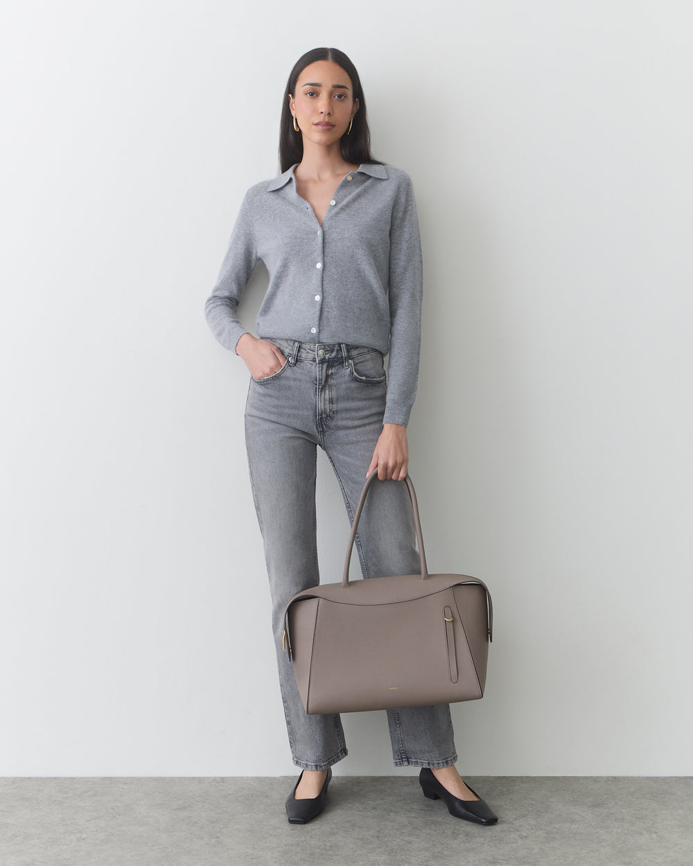 Person holding a tote bag wearing a buttoned shirt and jeans.