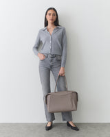 Person holding a tote bag wearing a buttoned shirt and jeans.