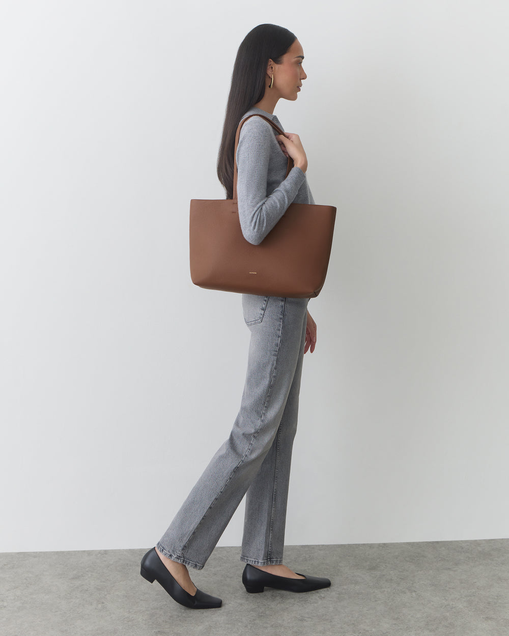 Person standing, holding a shoulder bag, wearing long-sleeve top and jeans.