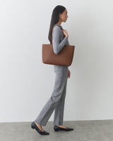 Person standing, holding a shoulder bag, wearing long-sleeve top and jeans.