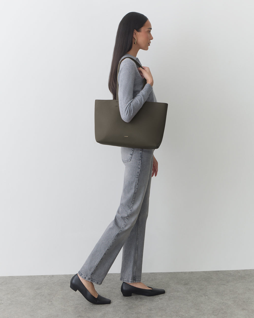 Person holding large handbag while standing against plain background.