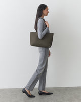 Person holding large handbag while standing against plain background.