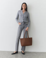Woman standing, wearing button-up shirt, jeans, flats, holding a shoulder bag.