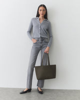 Person in casual outfit holding a tote bag, standing against a plain background.